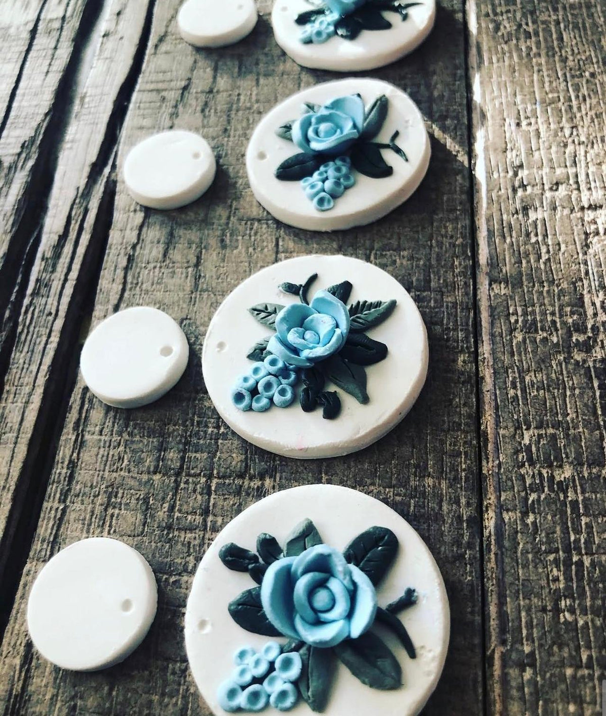 Blue Rose Drops: white round earring pieces with pale blue roses on dark wood